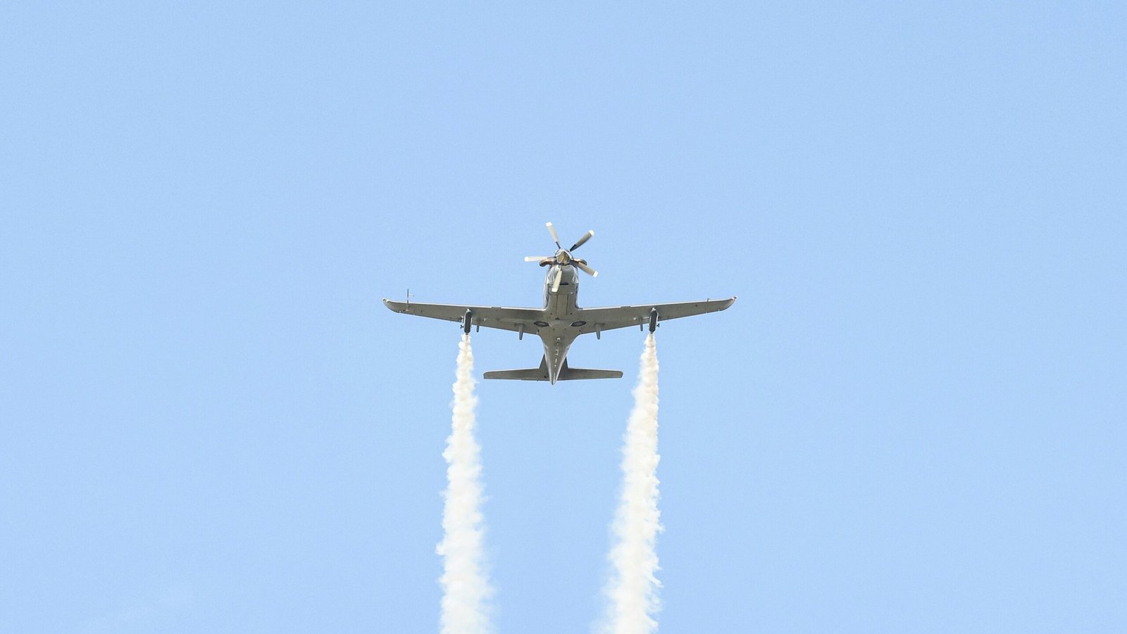 A plane flying in the air with two smoke trails behind it